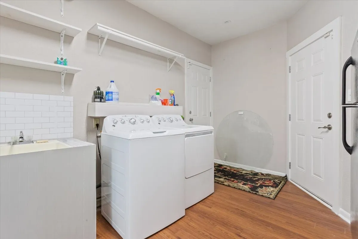 Utility sink with subway tile backsplash, wood-finish flooring, and white shelving