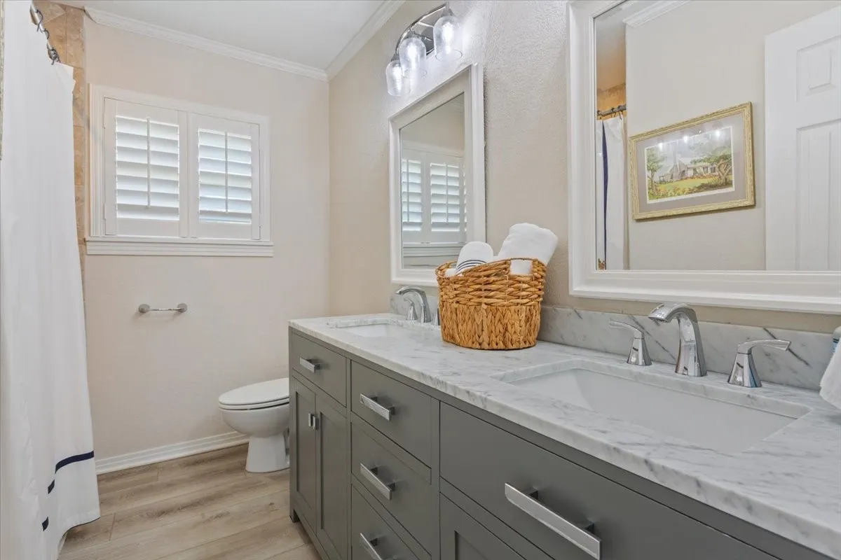 Dual vanity with gray cabinetry and chrome hardware, integrated rectangular sinks, and a marble-finish countertop
