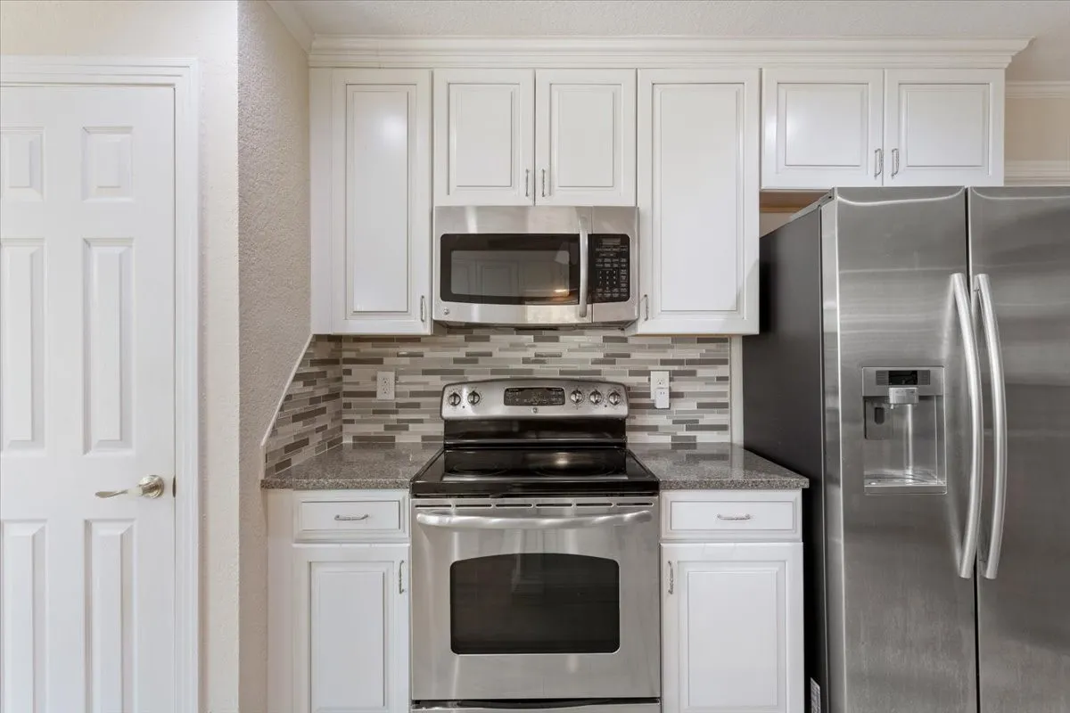 White cabinetry, stainless steel appliances, granite countertops, and a tiled backsplash