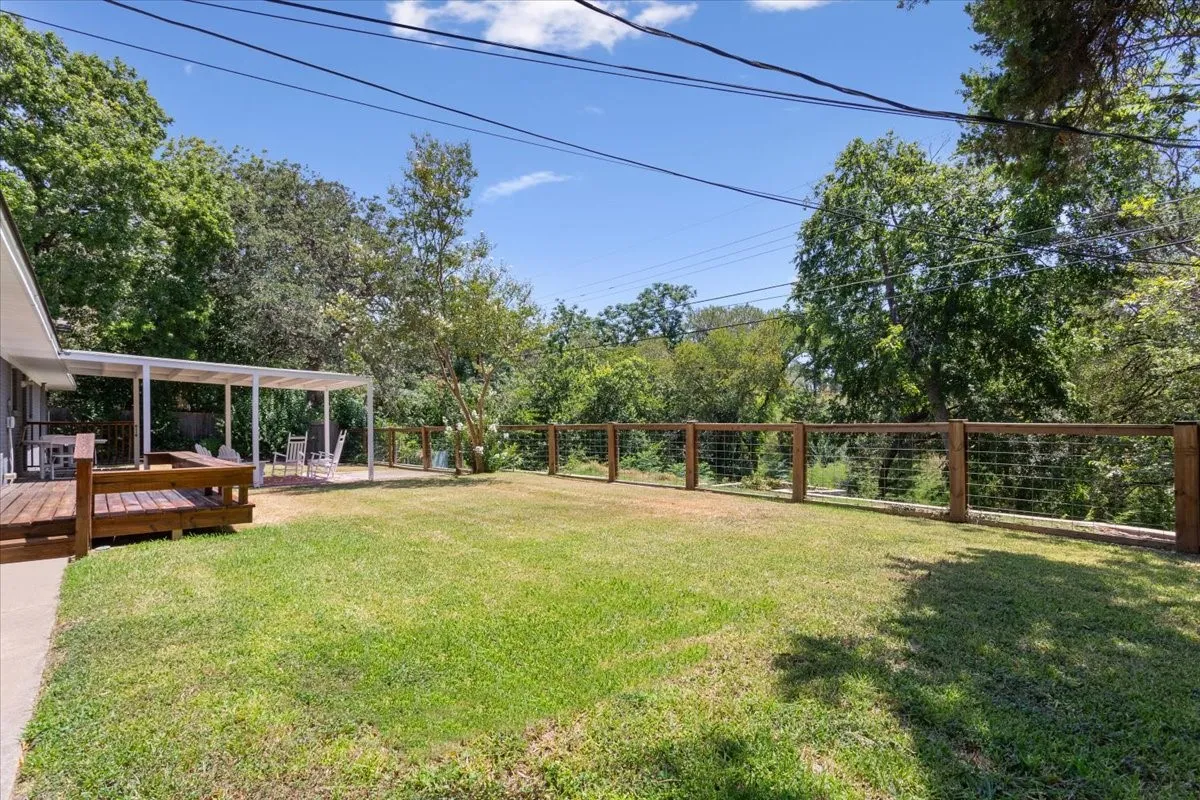 Expansive green lawn with a wood deck, covered patio, and wood post with cable fencing