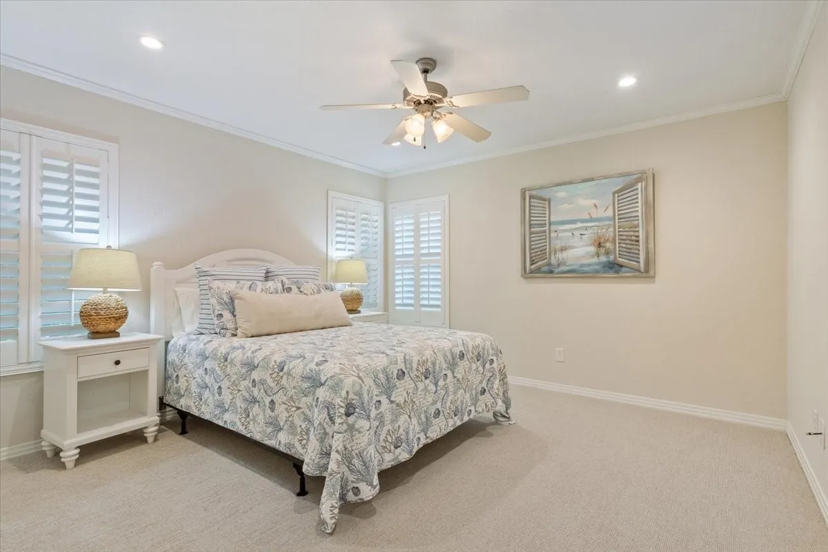 Recessed lighting, crown molding, ceiling fan, white plantation shutters, and light-toned carpeting