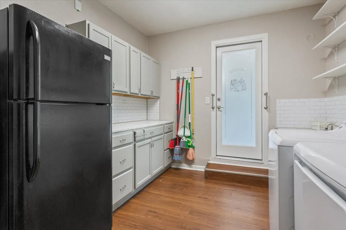 Laundry area featuring wood-finish flooring, white subway tile backsplash, white floating shelves, and a white frosted glass door