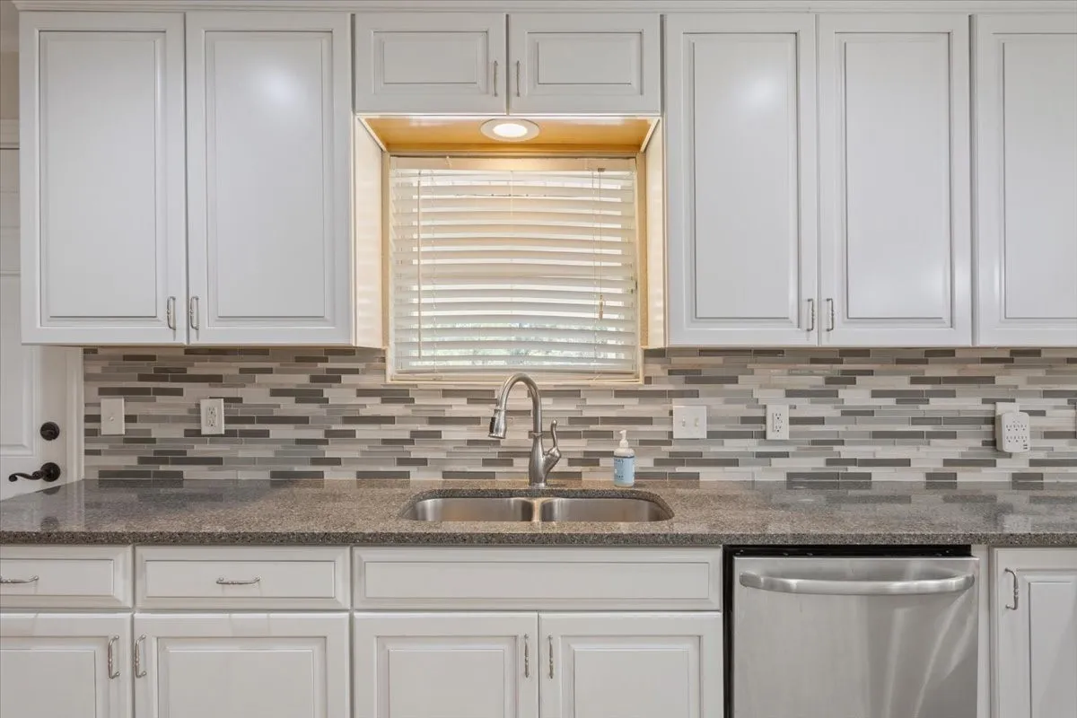 White cabinetry with brushed nickel hardware, multi-tone rectangular tile backsplash, dual basin stainless steel sink, gooseneck faucet, and stainless steel dishwasher