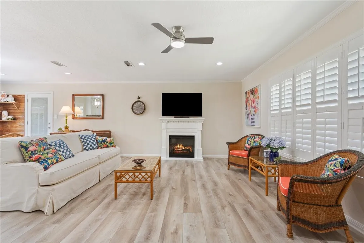 Living area featuring wood-finish flooring, a contemporary ceiling fan with integrated lighting, recessed lighting, white window shutters, and a built-in fireplace with a white mantel