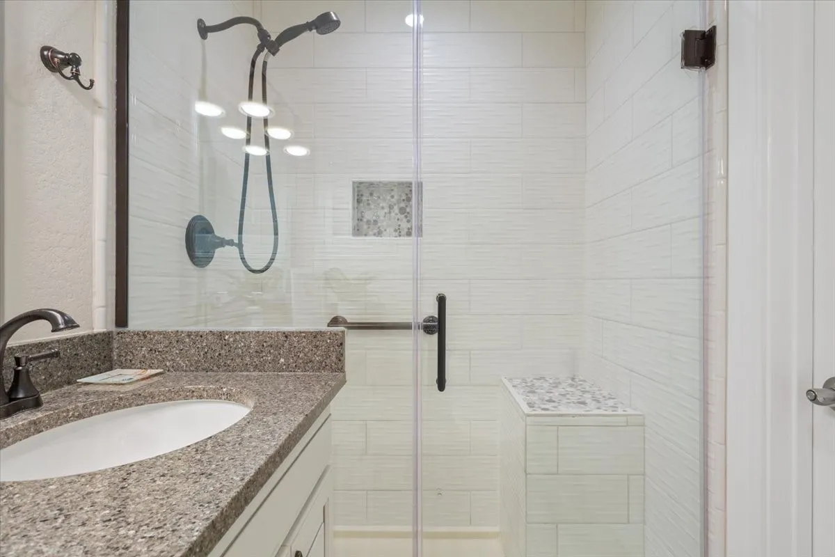 Frosted glass shower enclosure, built-in shower bench, recessed shower niche, oil-rubbed bronze shower fixtures, and a vanity with a stone-finish countertop