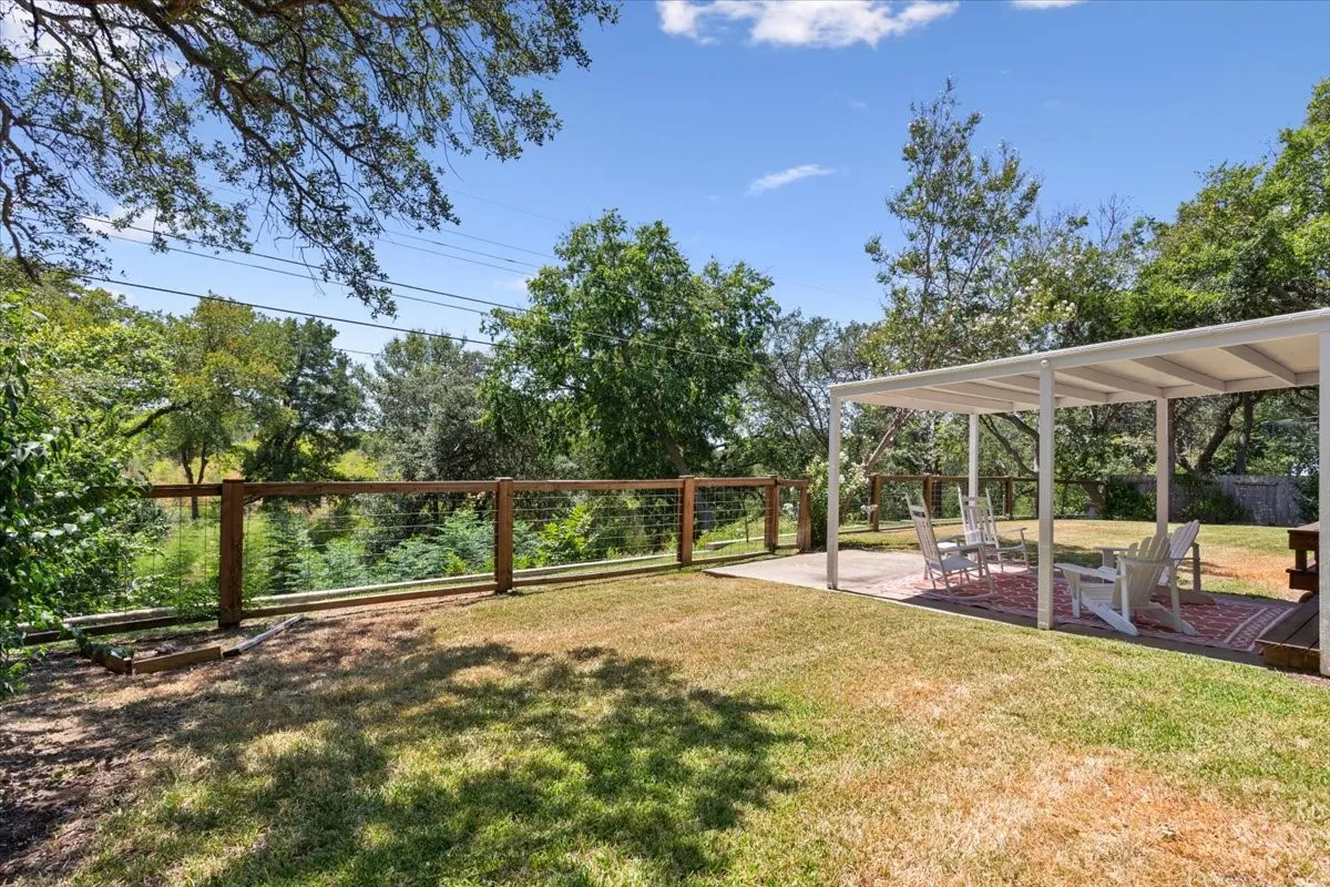 Expansive grassy area with a covered patio, concrete hardscaping, and a wood and wire fence