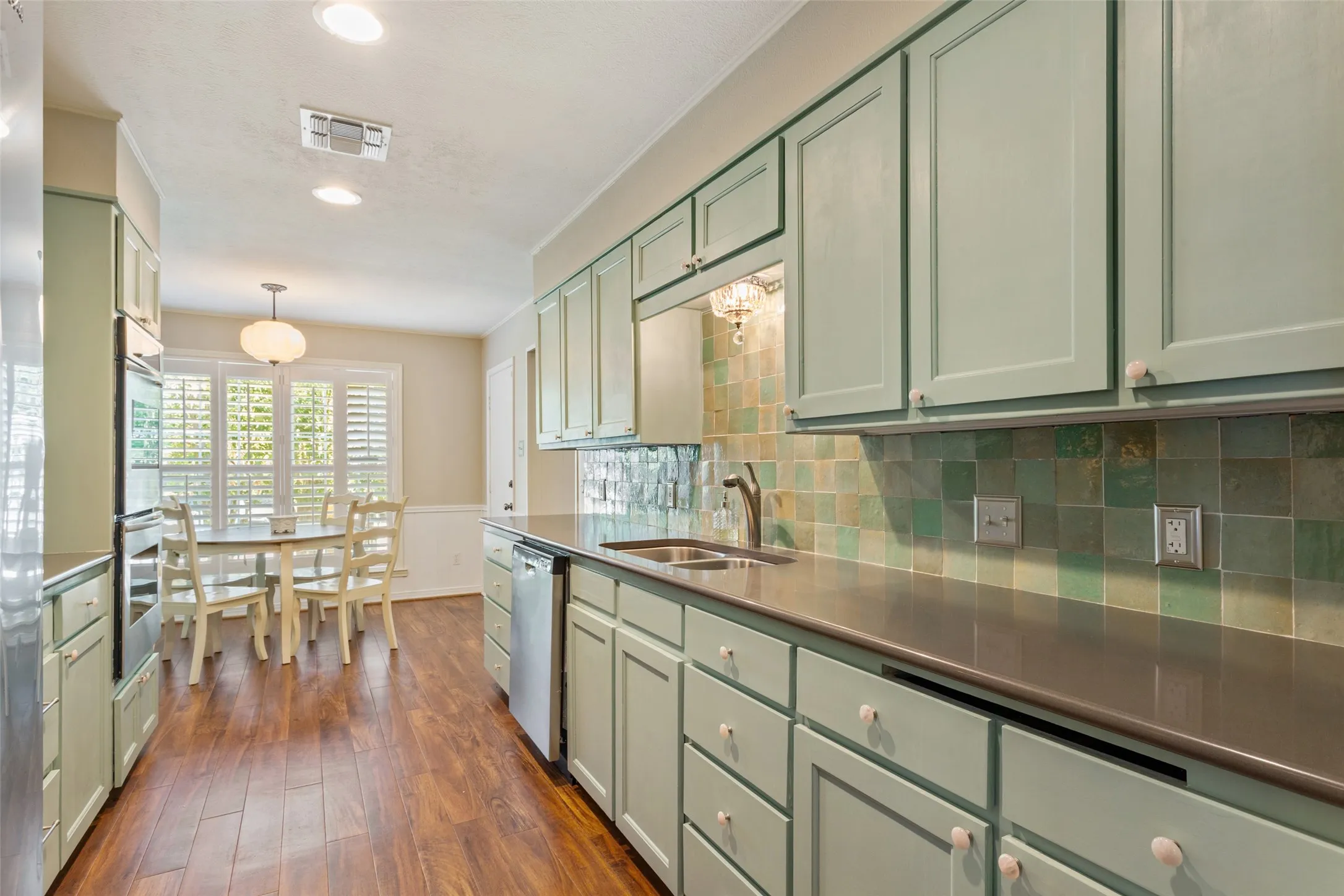 Kitchen featuring light green cabinetry, dark countertops, a tiled backsplash, wood-finish flooring, and recessed lighting