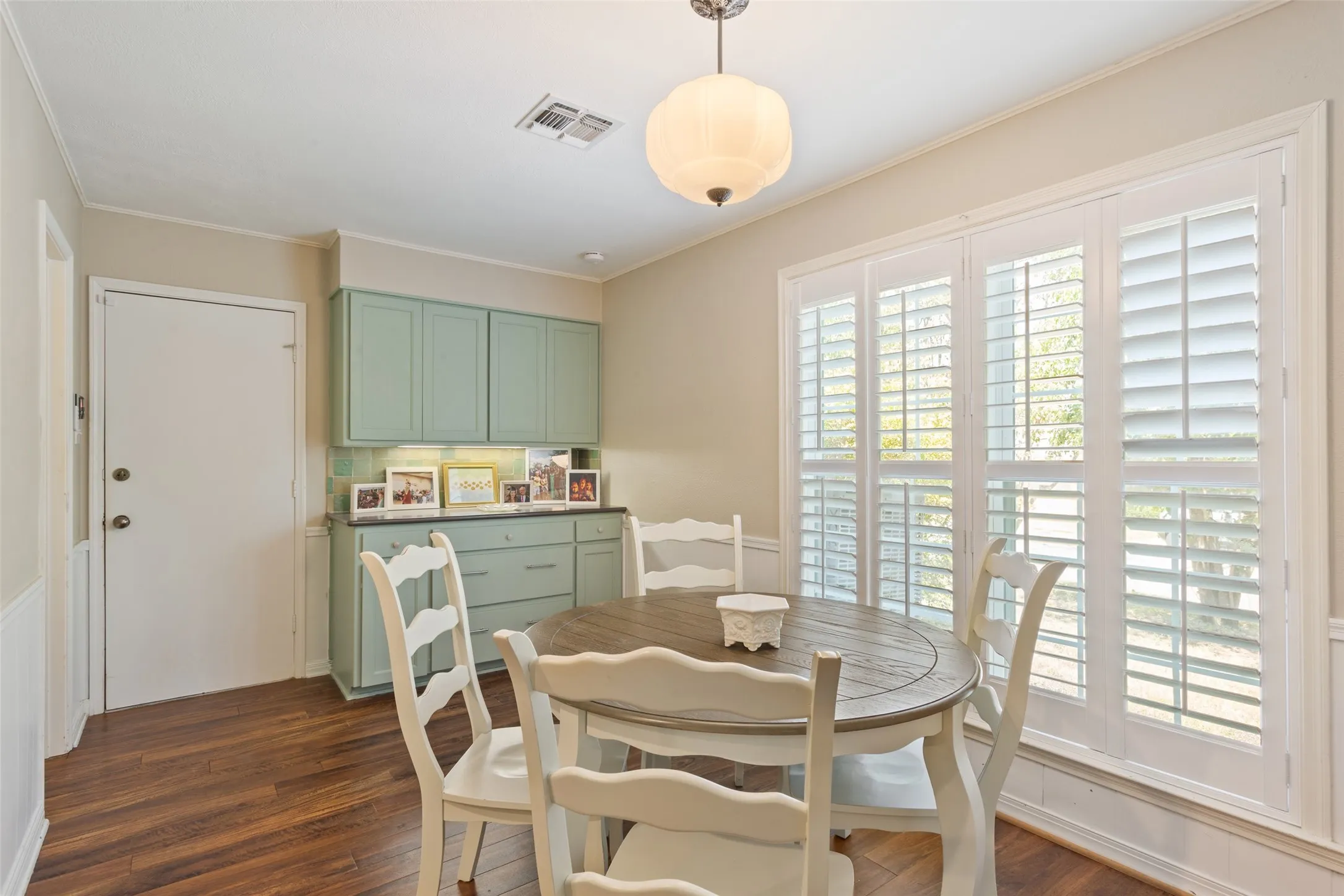 Bright dining area featuring a wood-finish oval table, ladder-back chairs, and abundant natural light from plantation shutter-style glass doors
