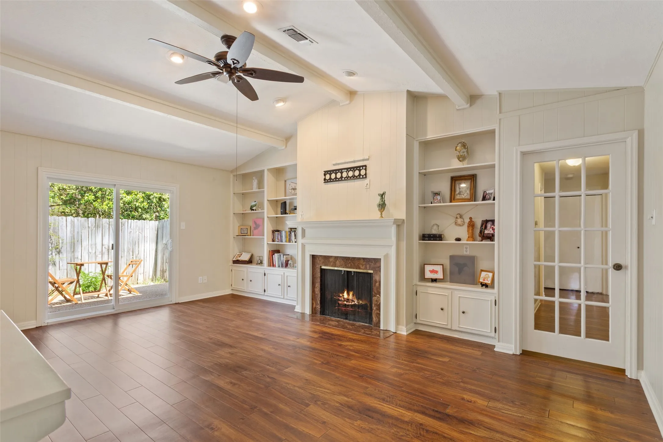 Vaulted ceiling with exposed beams, wood-finish flooring, built-in shelving, fireplace with stone surround, and a glass-paned door