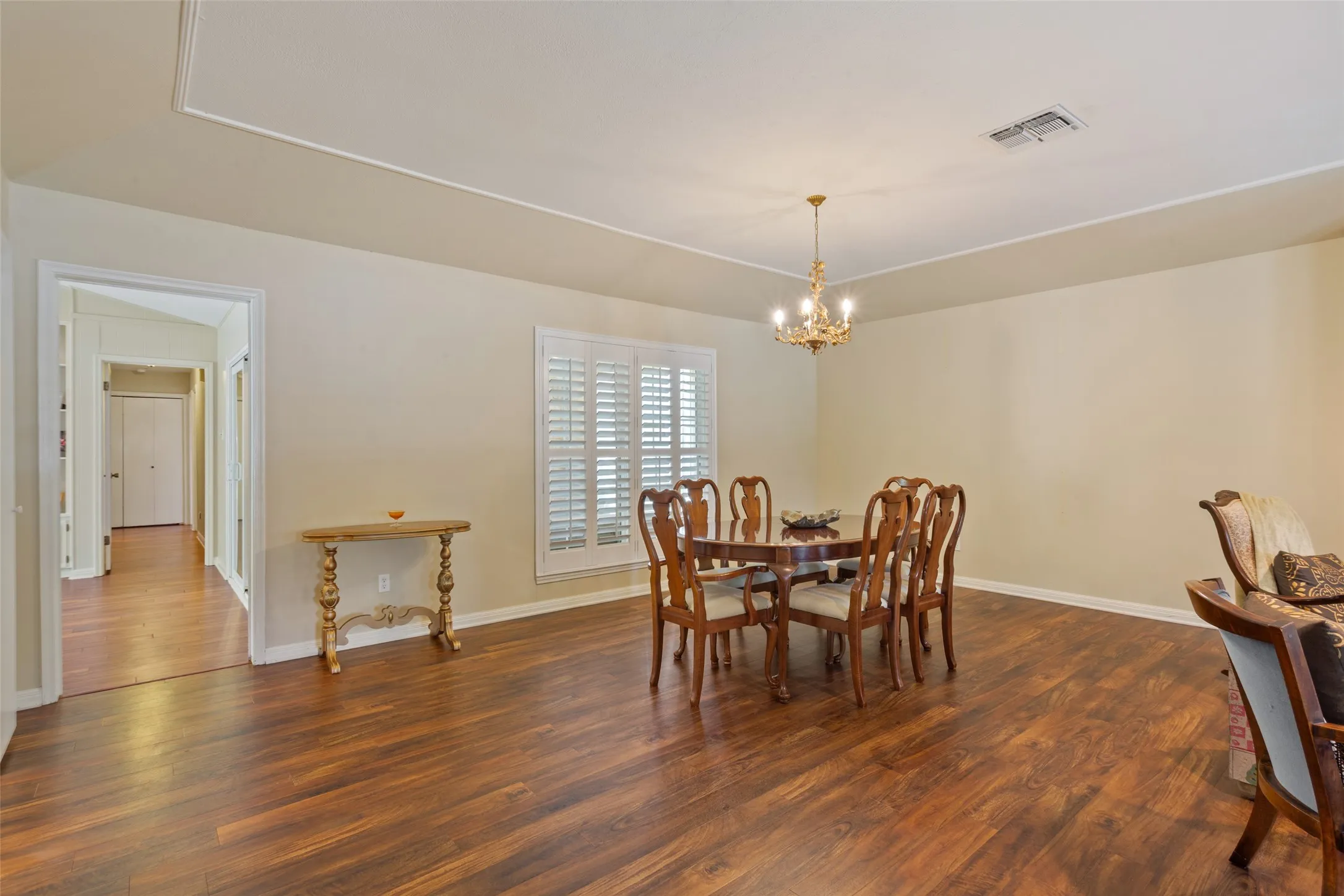 Recessed ceiling with decorative molding, wood-finish flooring, window with plantation shutters, and a chandelier