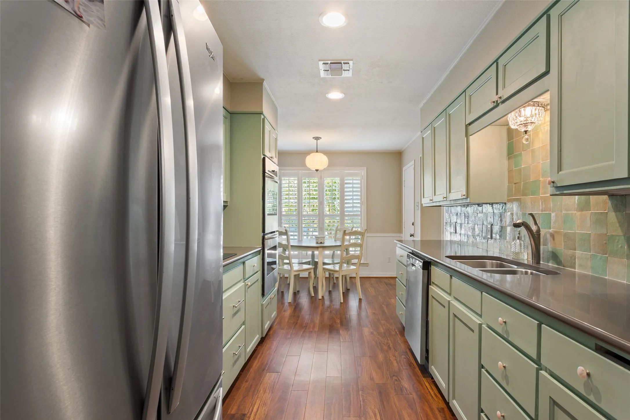 Galley kitchen featuring wood-finish flooring, custom cabinetry, stainless steel appliances, and a tile backsplash