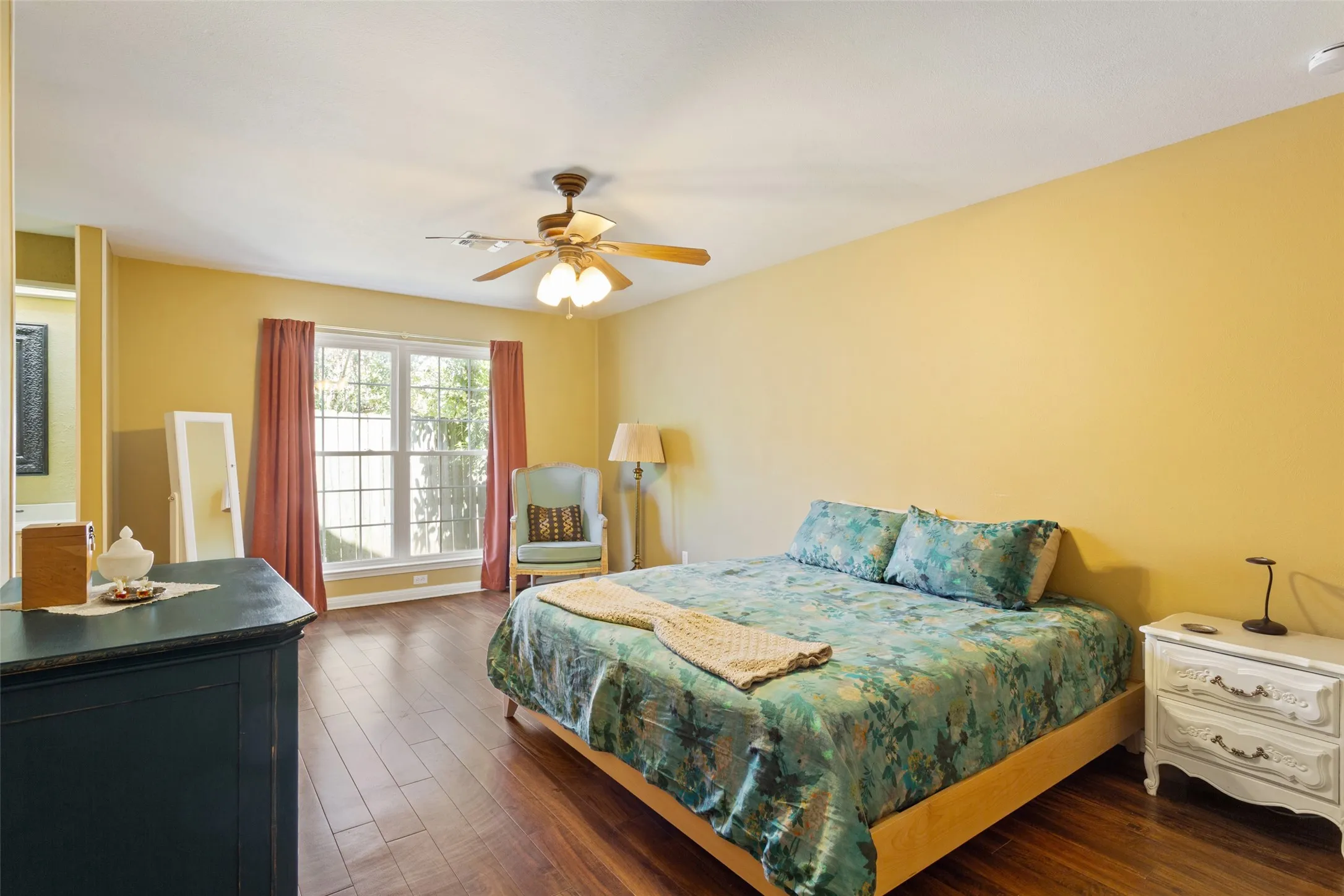 Wood-finish flooring, ceiling fan, and window with exterior greenery visible