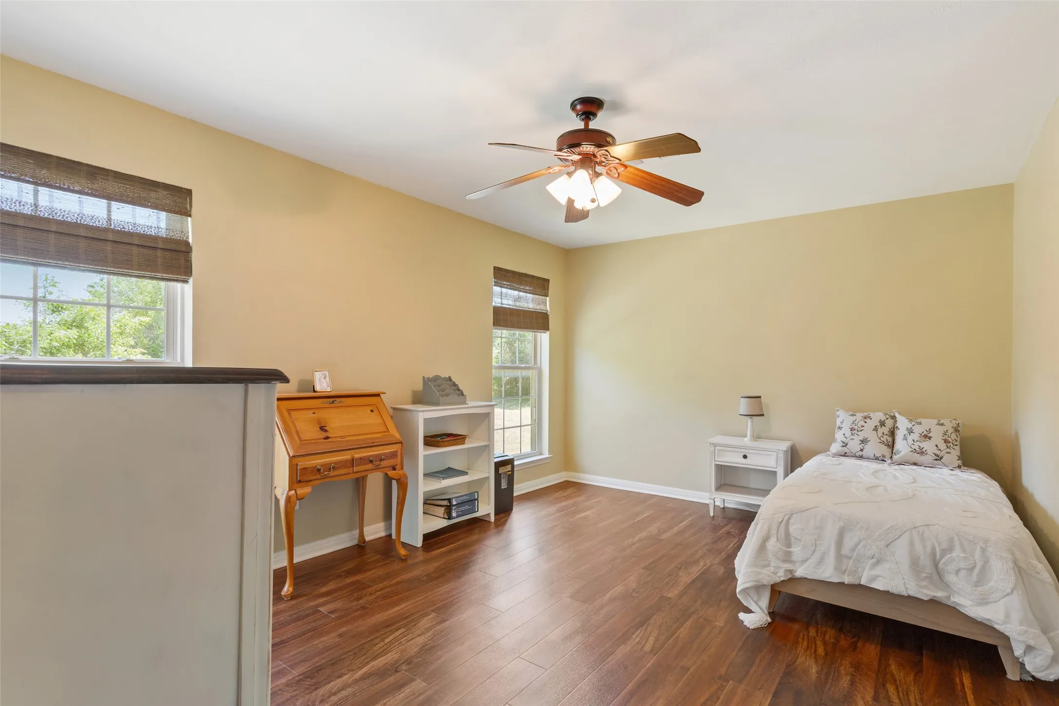 Wood-finish flooring, multiple windows with blinds, ceiling fan with integrated lighting, and a built-in half-wall partition
