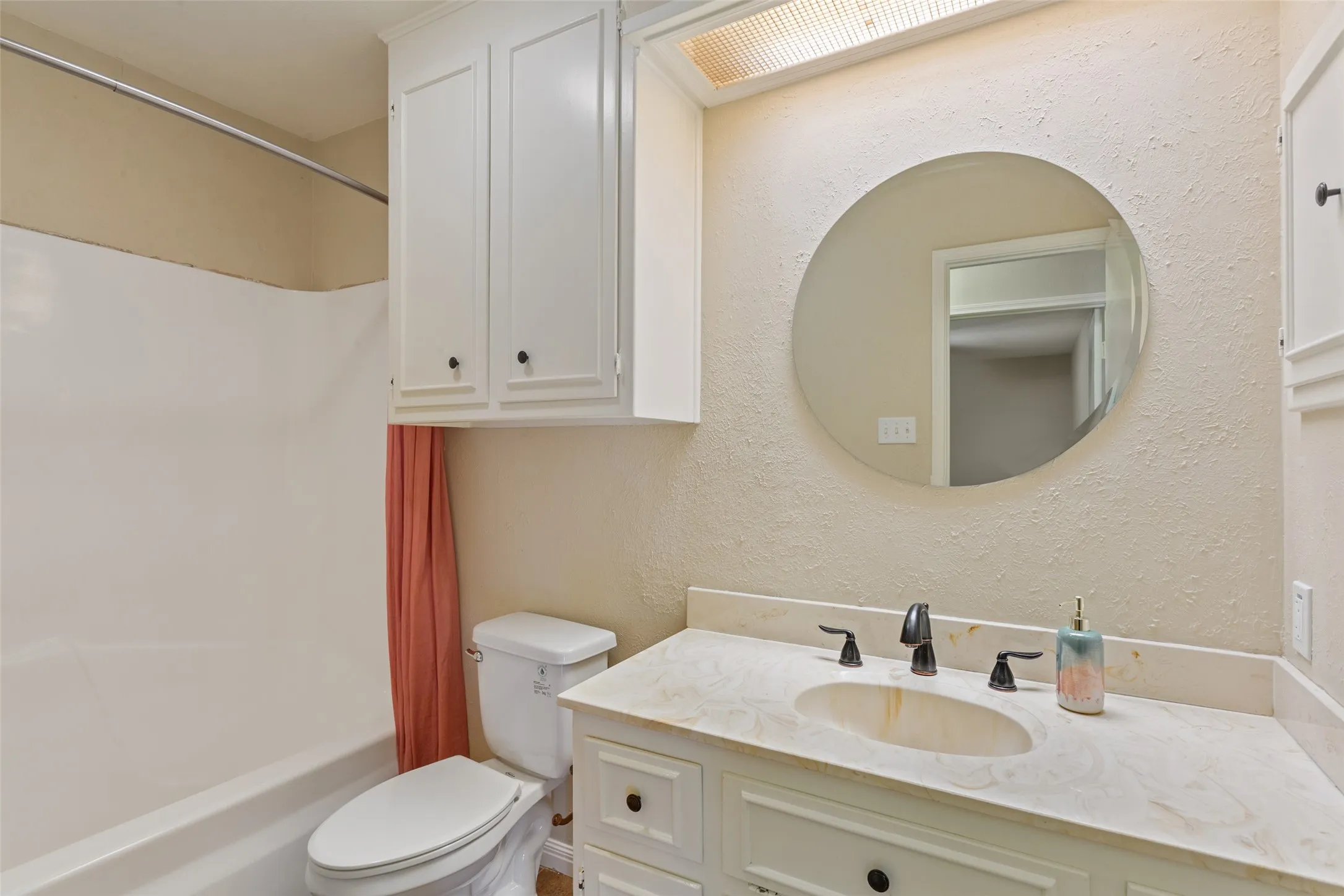 Vanity with an integrated sink, built-in cabinetry, a round mirror, and a built-in tub and shower