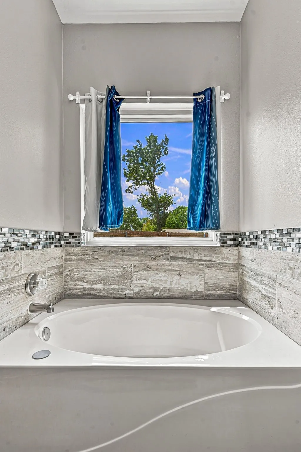 Built-in bathtub with chrome fixtures, surrounded by large format tile and a decorative mosaic border