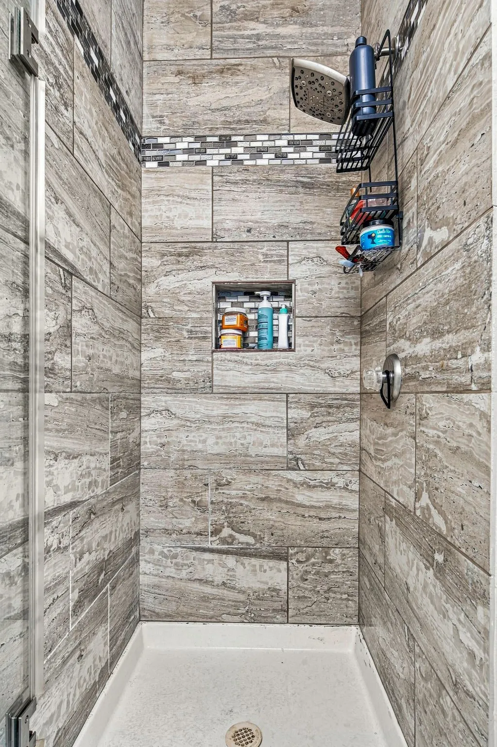 Shower enclosure featuring wood-look wall tile, a decorative mosaic tile accent, a recessed niche, and a white shower pan