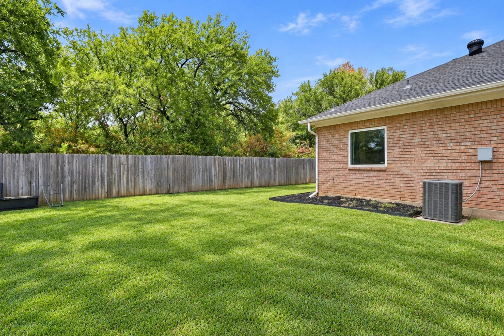 Expansive green lawn, brick exterior, dark composition shingle roof, white window trim, and wood privacy fencing