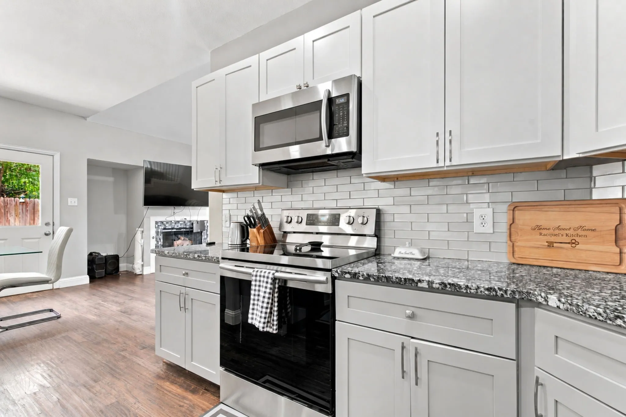 White shaker-style cabinetry, stainless steel appliances, speckled stone countertops, and a white subway tile backsplash