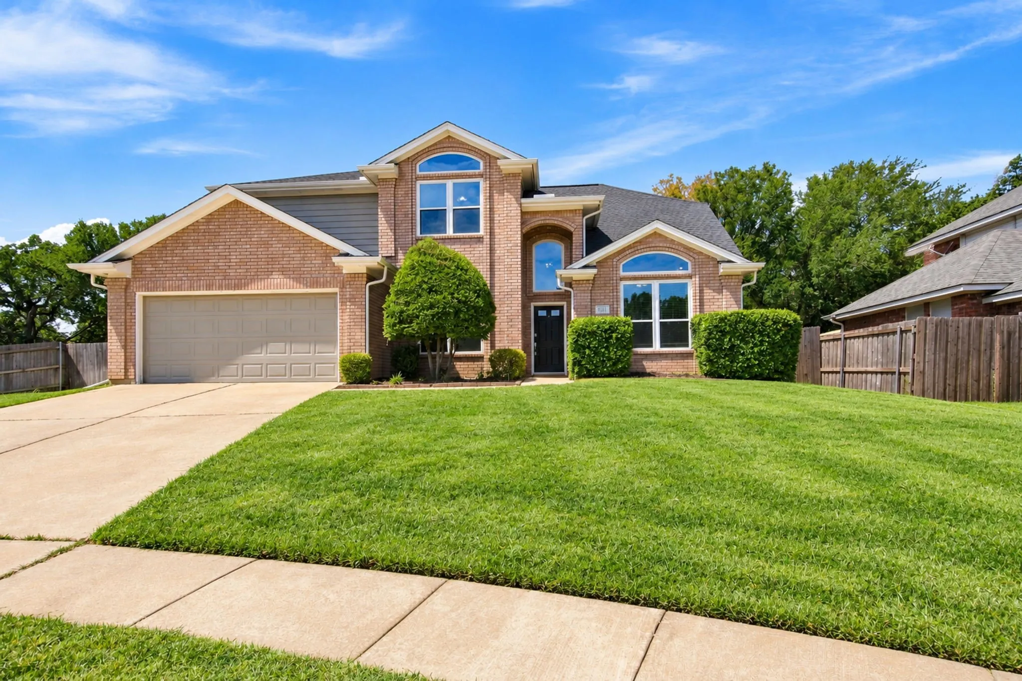 Brick and siding exterior featuring an arched entryway, multiple windows, a two-car garage, and a concrete driveway