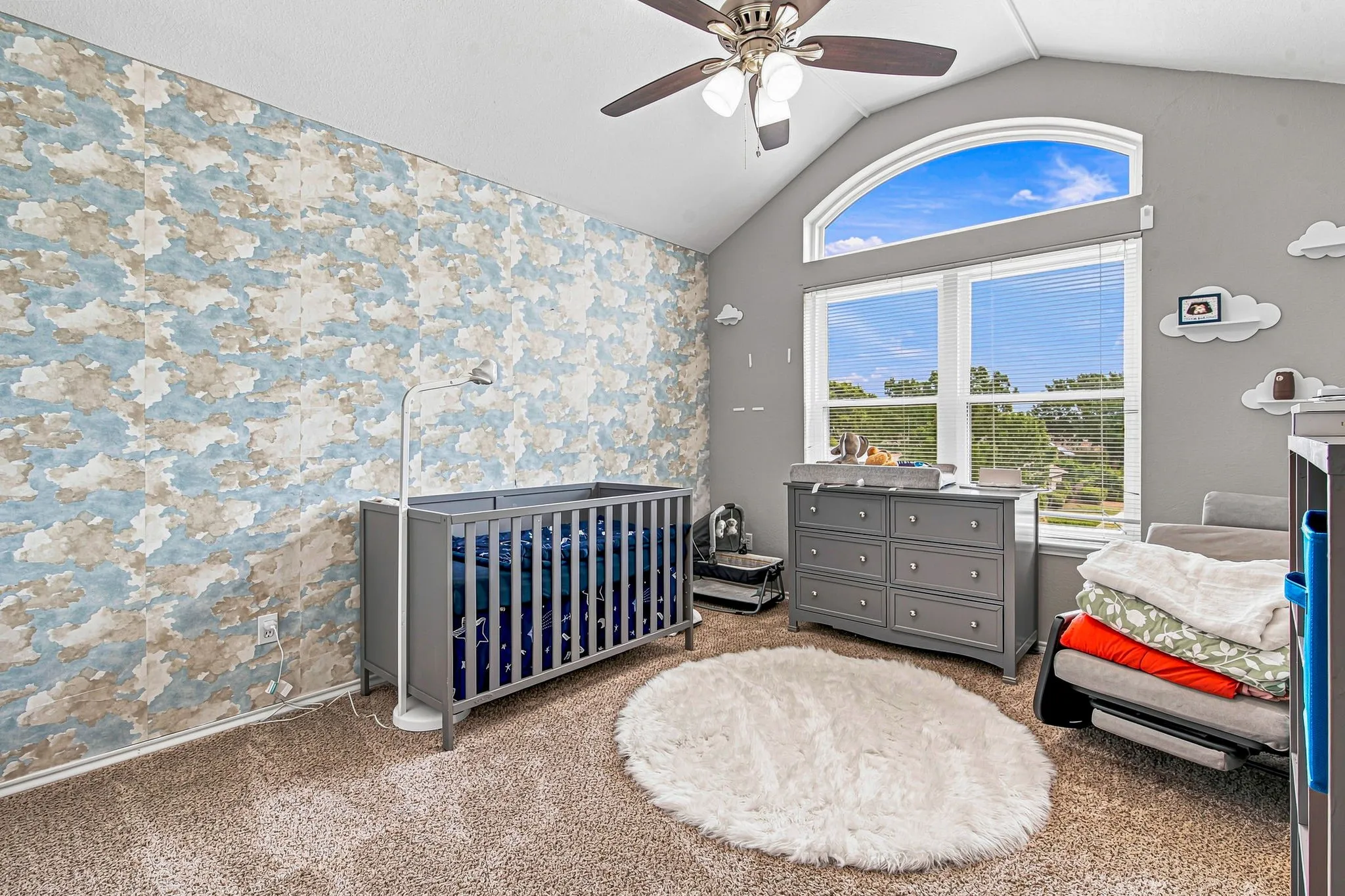 Vaulted ceiling with ceiling fan, large arched window, textured wall covering, and neutral carpeting