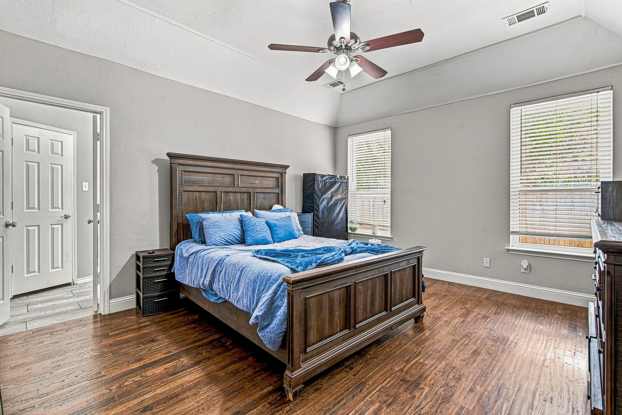 Tray ceiling, wood-finish flooring, ceiling fan with integrated lighting, and dual windows with blinds