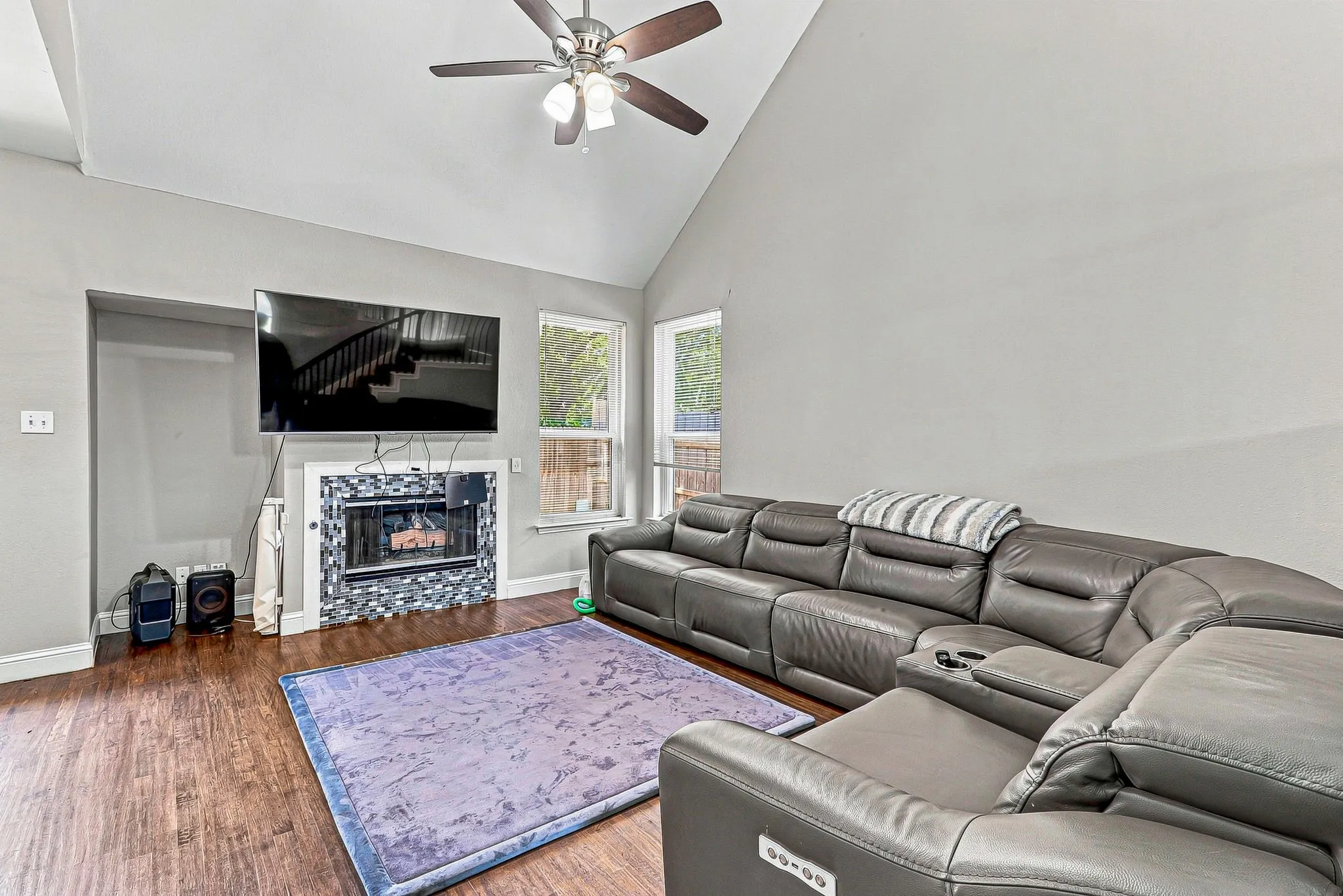 Vaulted ceiling with a ceiling fan, wood-finish flooring, and a fireplace with a decorative tile surround