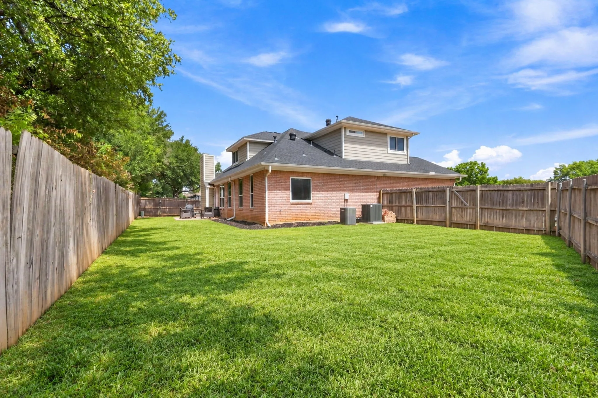 Expansive grass lawn bordered by a wood fence, featuring a brick exterior and a two-story structure with siding