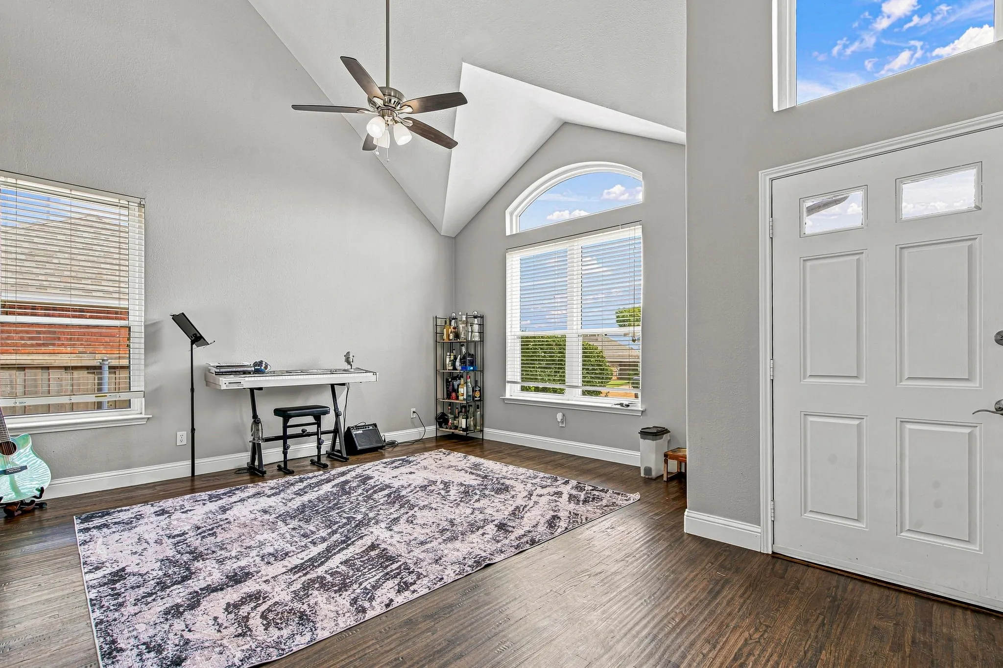 Vaulted ceiling, ceiling fan, rich wood-finish flooring, white paneled door, and a large arched window