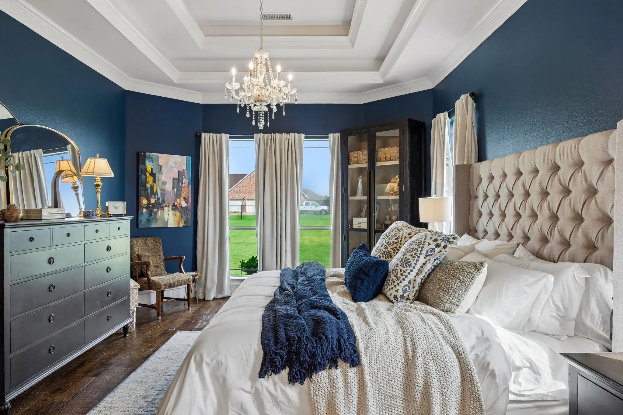 Another view of the primary bedroom featuring a tiered tray ceiling with a chandelier