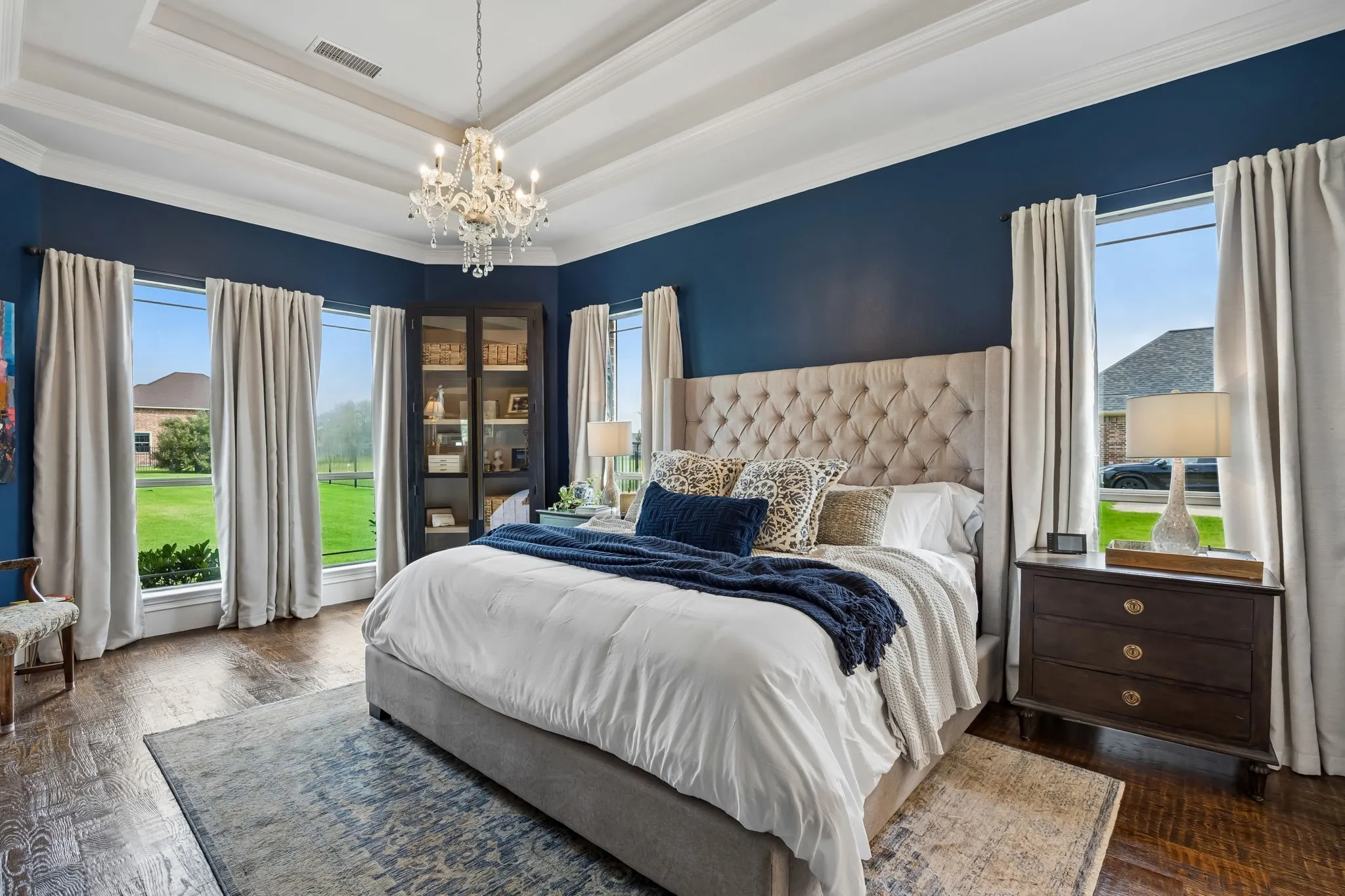 Spacious primary bedroom room with wood-finish flooring, a tray ceiling, and a chandelier