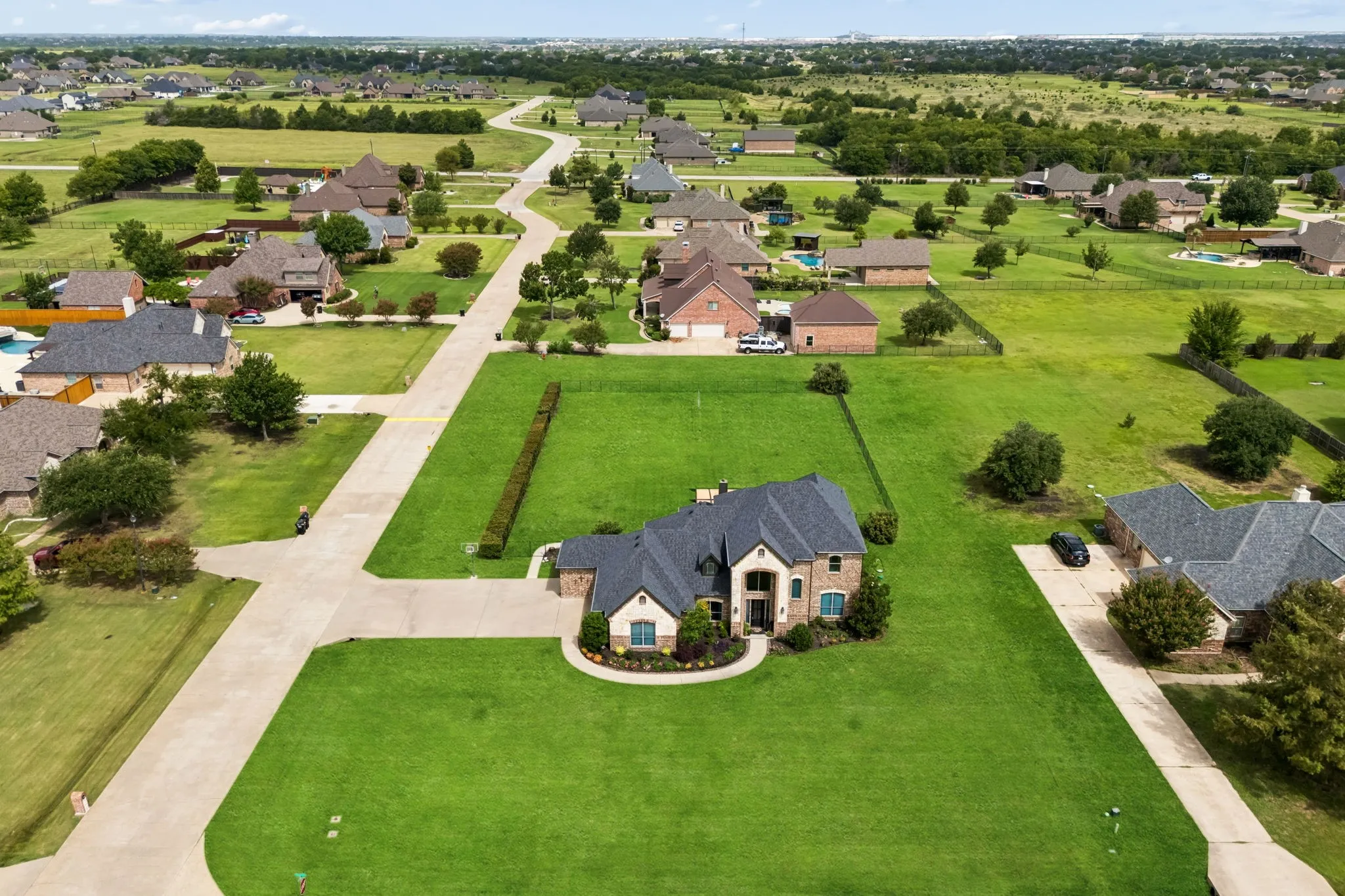 Expansive green lawn surrounds a traditional brick residence with a dark shingle roof