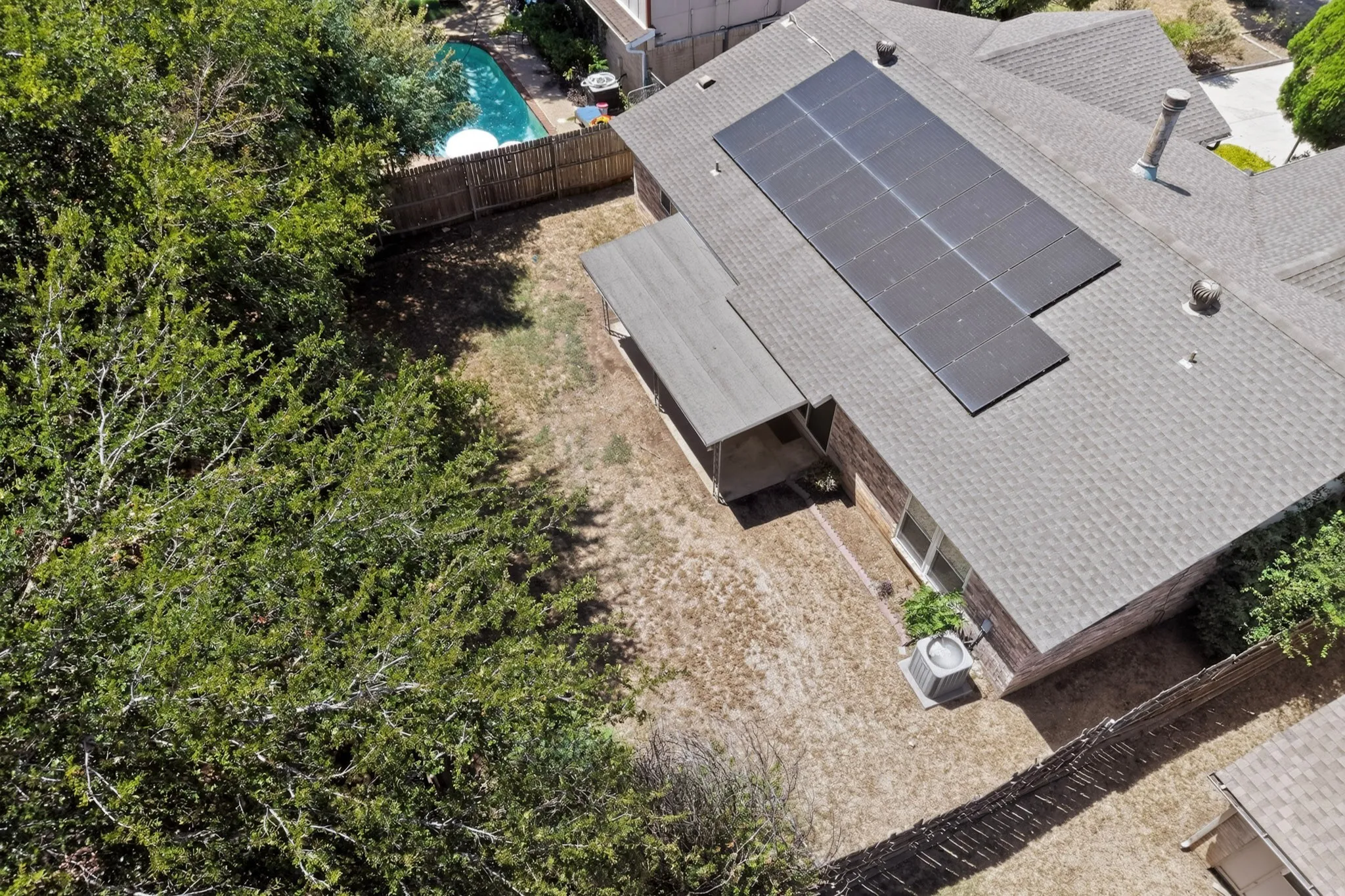 Shingled roof with solar panel array, brick exterior, fenced backyard, and covered patio