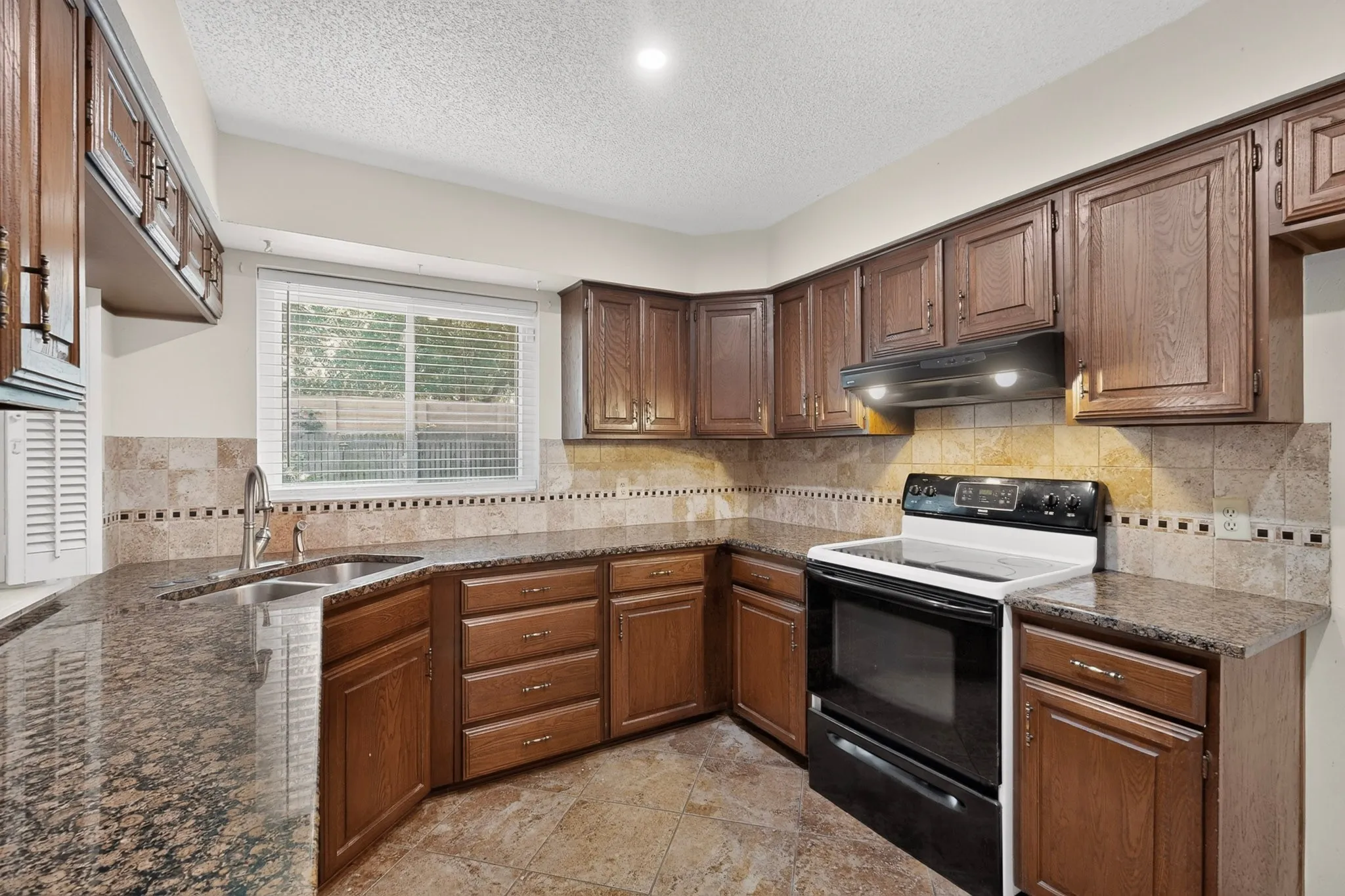 Kitchen featuring wood cabinetry, solid surface countertops, tile backsplash, stainless steel sink, and tile flooring
