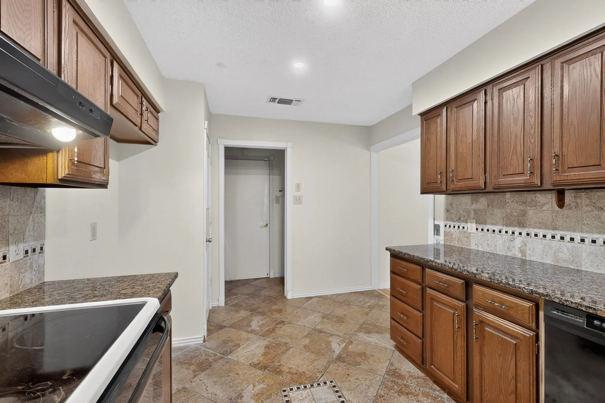 Kitchen featuring wood cabinetry, dark countertops, tiled backsplash with decorative accent, and tiled flooring
