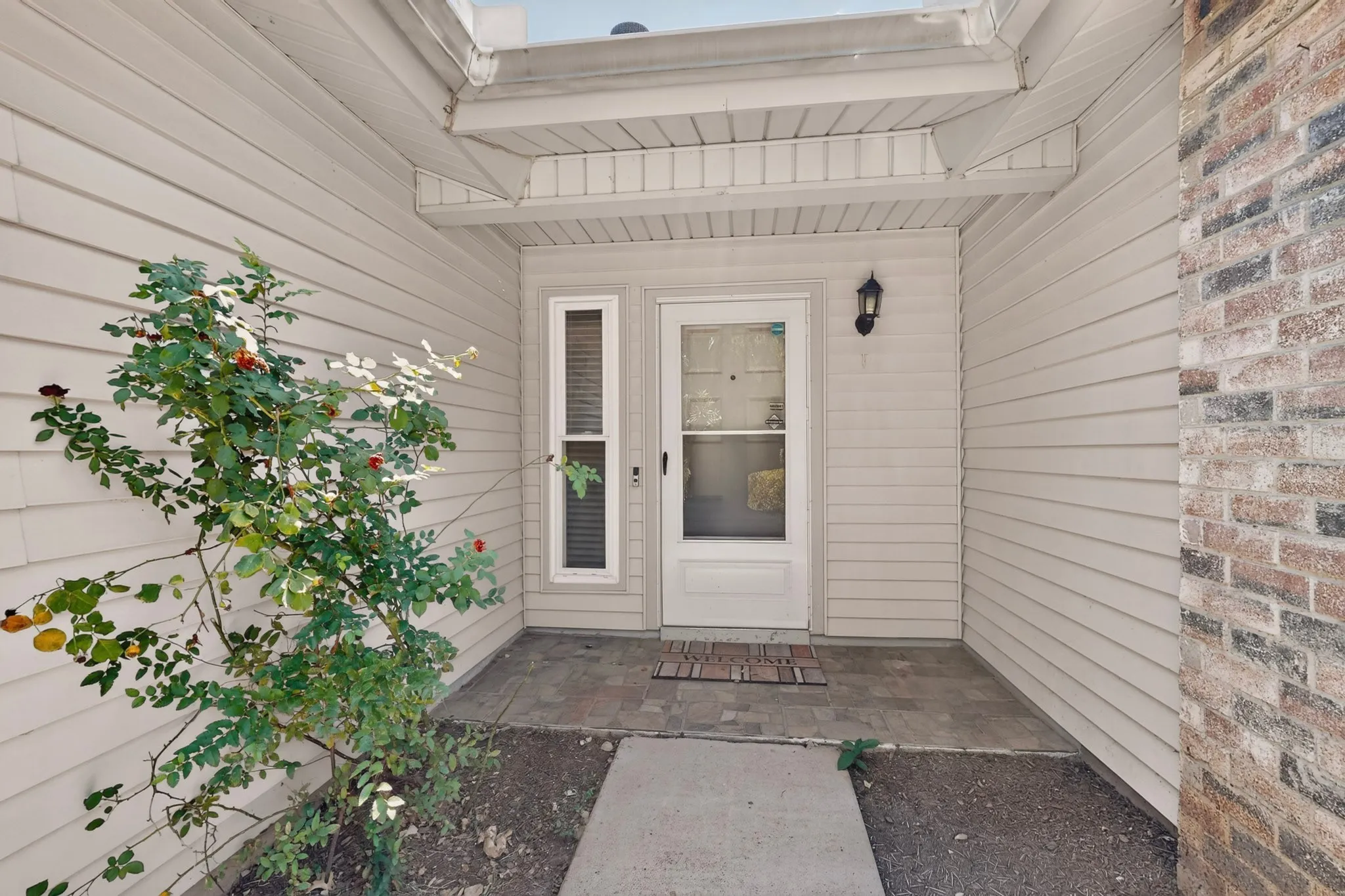 Front entry with a white storm door, vertical side light, and an exterior wall lantern