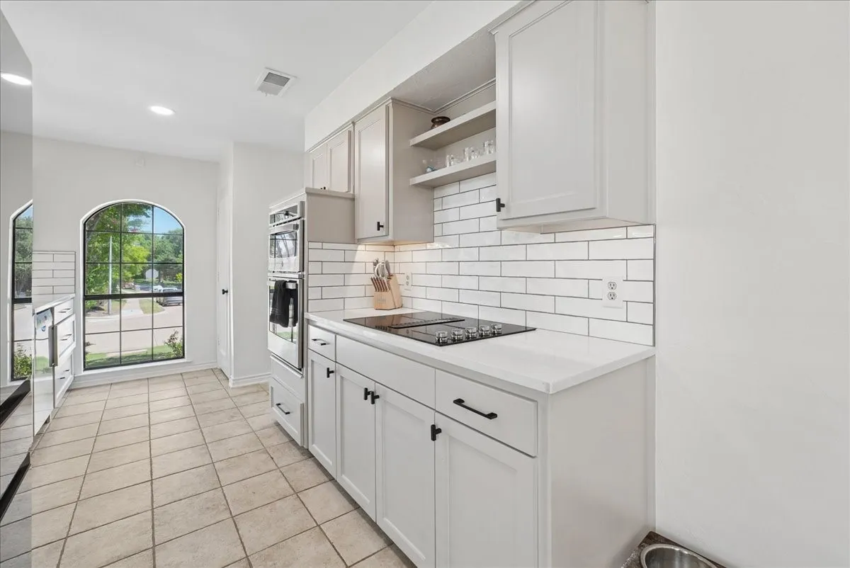 Kitchen featuring white shaker-style cabinetry, white subway tile backsplash, light-toned tile flooring, built-in double ovens, and a black cooktop