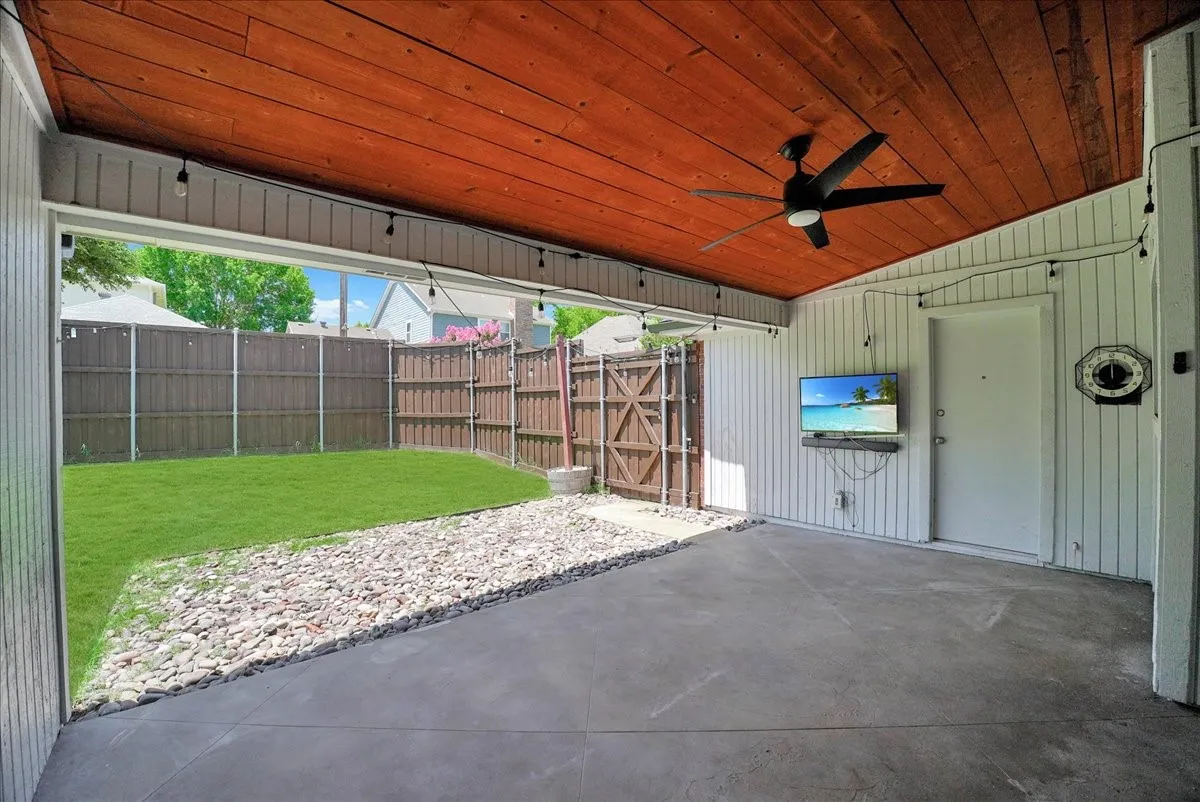 Covered patio featuring a wood-panel ceiling, dark-finish ceiling fan, and string lighting