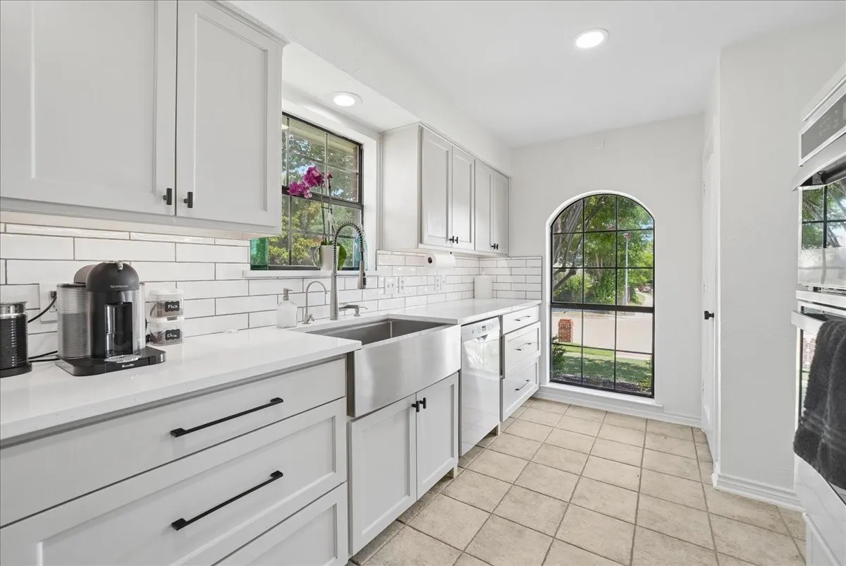 Kitchen featuring white shaker-style cabinetry, a stainless steel farmhouse sink, white subway tile backsplash, and light-toned tile flooring