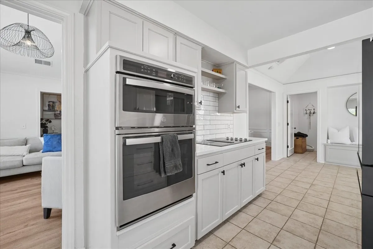 Modern kitchen featuring light-toned cabinetry with matte black hardware, stainless steel built-in double ovens, a built-in cooktop, and subway tile backsplash