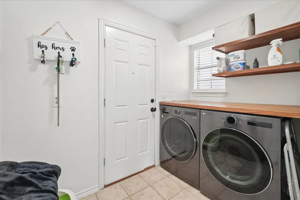Dedicated laundry area featuring a wood-finish countertop, integrated shelving, and tiled flooring