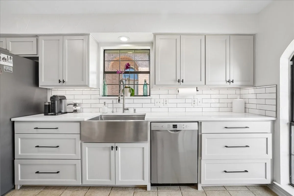 Contemporary kitchen featuring light-toned cabinetry with dark hardware, white countertops, and a subway tile backsplash