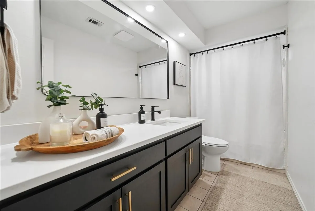 Contemporary bathroom featuring a dark wood-finish vanity with gold-tone hardware, a white countertop, and a rectangular undermount sink with a matte black faucet