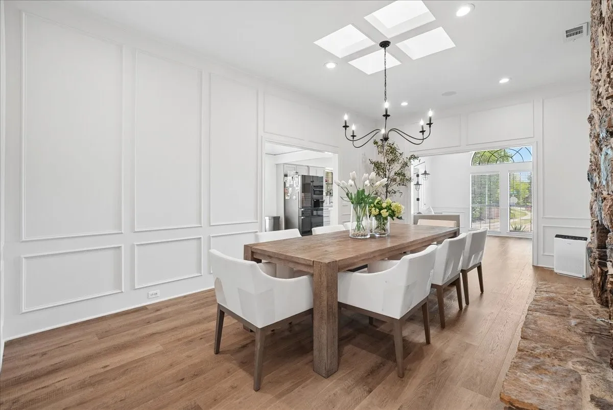 Bright room with wood-finish flooring, featuring decorative wall molding, a stone-clad fireplace, and an arched French door leading to the exterior
