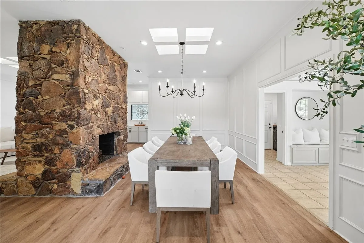Dining area featuring a prominent floor-to-ceiling stone fireplace, wood-finish flooring, and white wall paneling