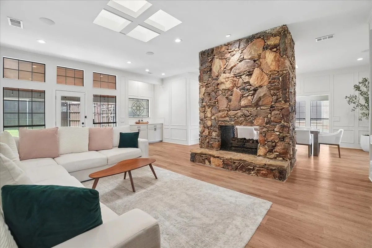 Spacious living area featuring a prominent stone fireplace, wood-finish flooring, multiple skylights, and a wall of windows and glass doors
