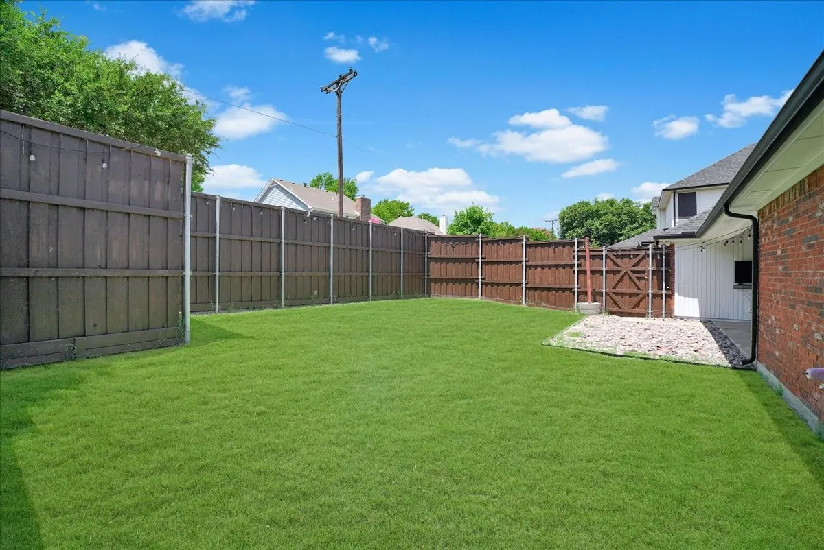 Expansive fenced yard featuring a large grass area, a rock bed, and a wooden gate