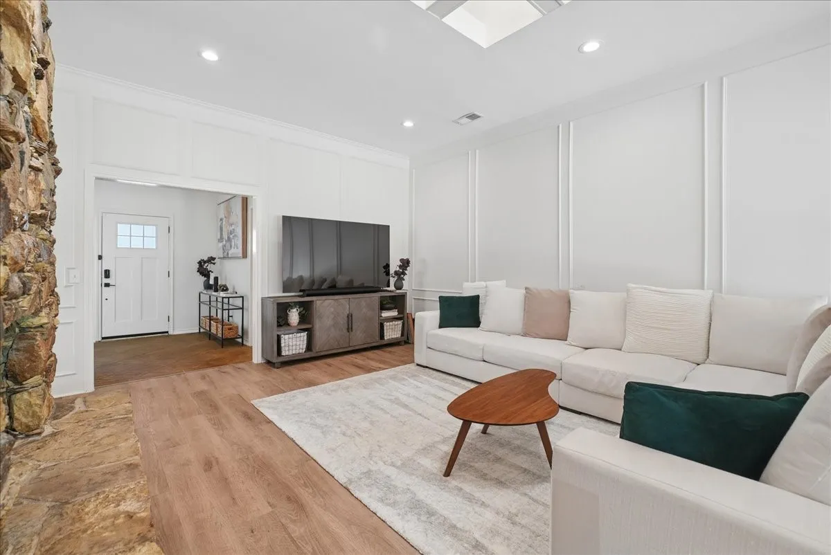 Spacious living area featuring light wood-finish flooring, recessed lighting, and white paneled walls