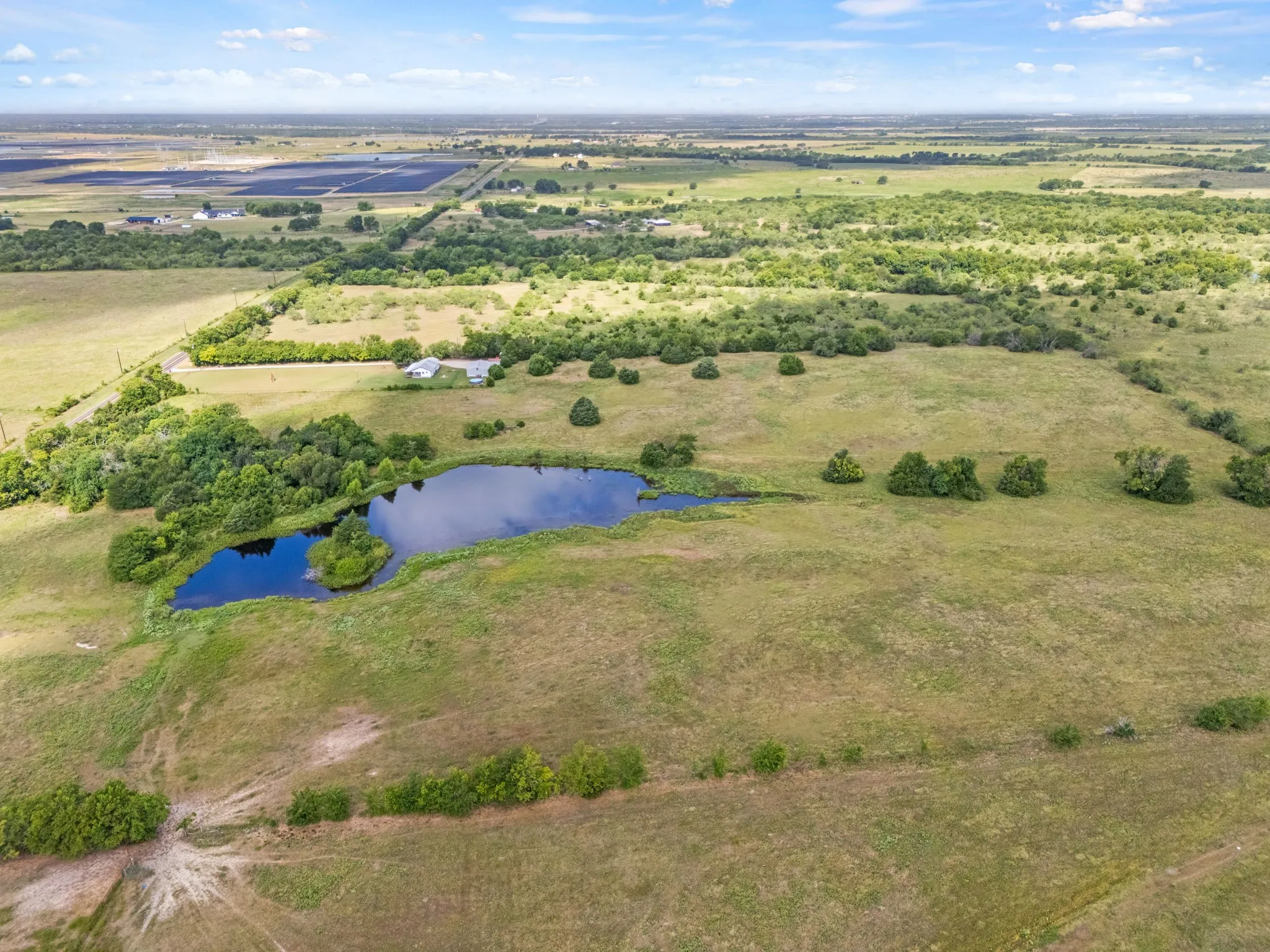 Expansive acreage featuring a private pond with a small island, surrounded by scattered trees and open fields