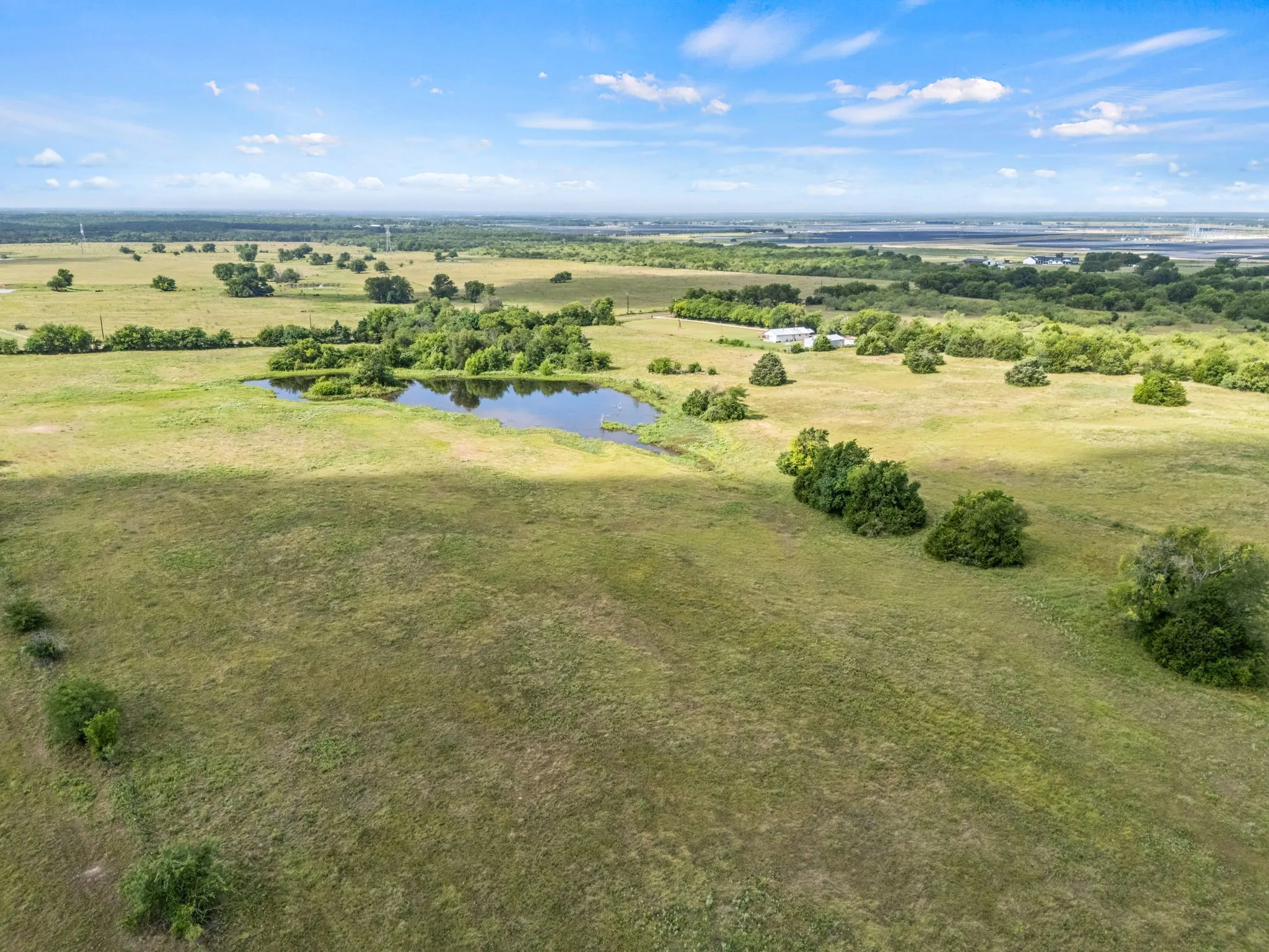 Expansive rural landscape featuring a natural pond, scattered mature trees, and open grassy areas