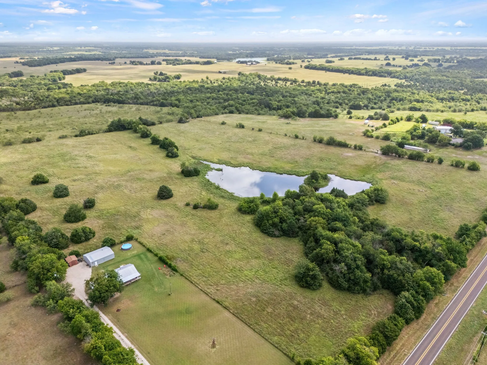 Expansive green acreage featuring a private pond, open fields, and mature trees